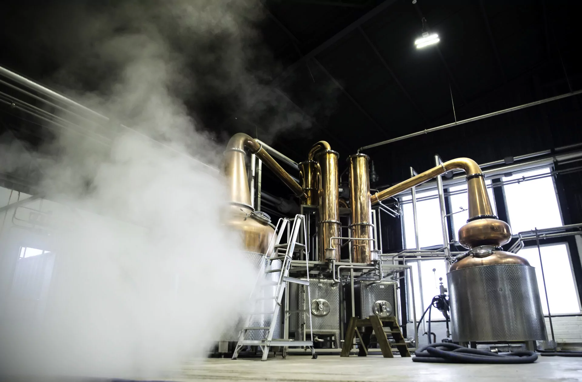 Industrial interior of a renewable energy distillery featuring large copper pots and stainless steel tanks powered by green hydrogen technology