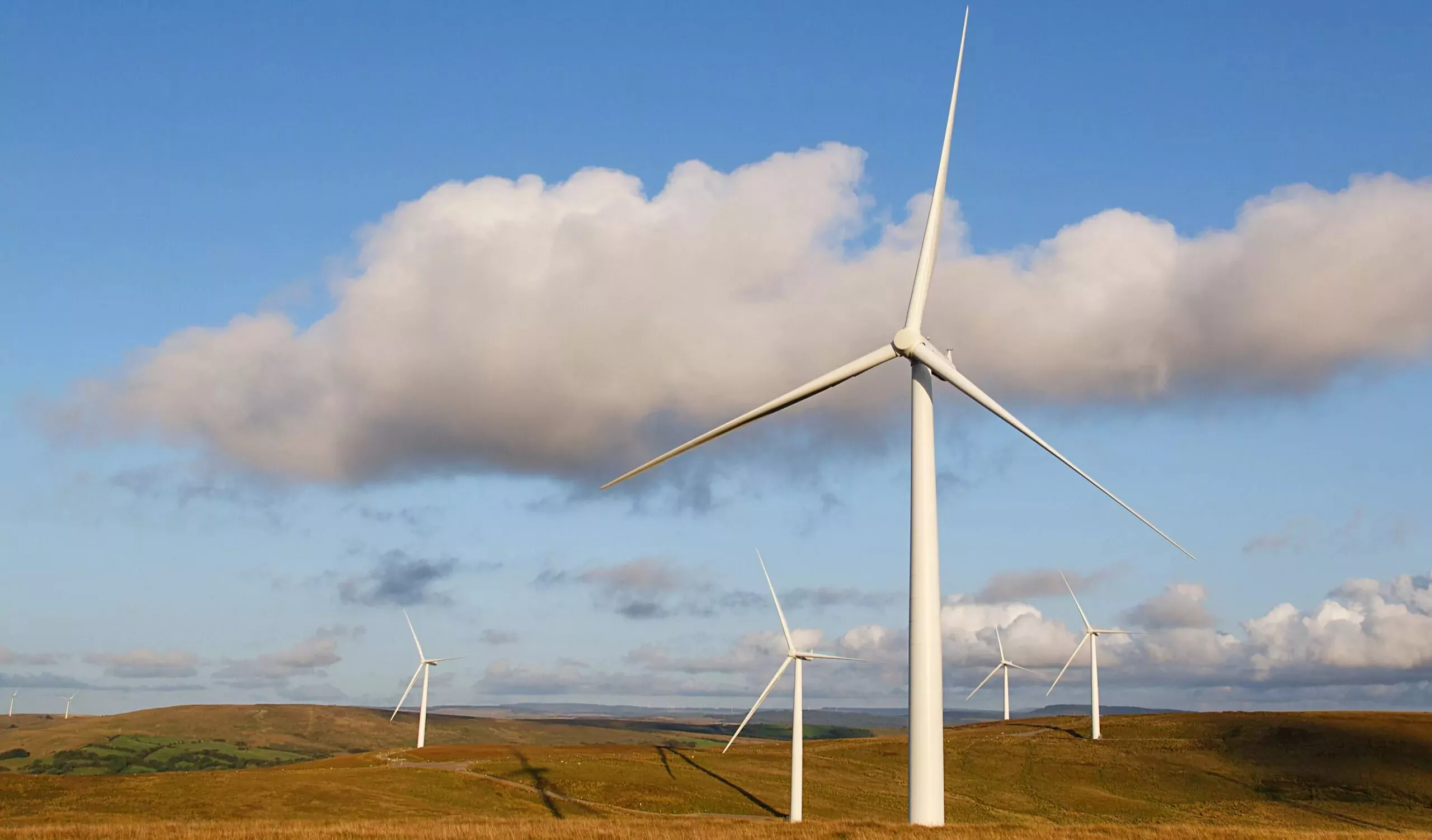 “Onshore wind turbines installed across rolling rural farmland in the UK, forming a wind farm within an open countryside landscape generating renewable energy